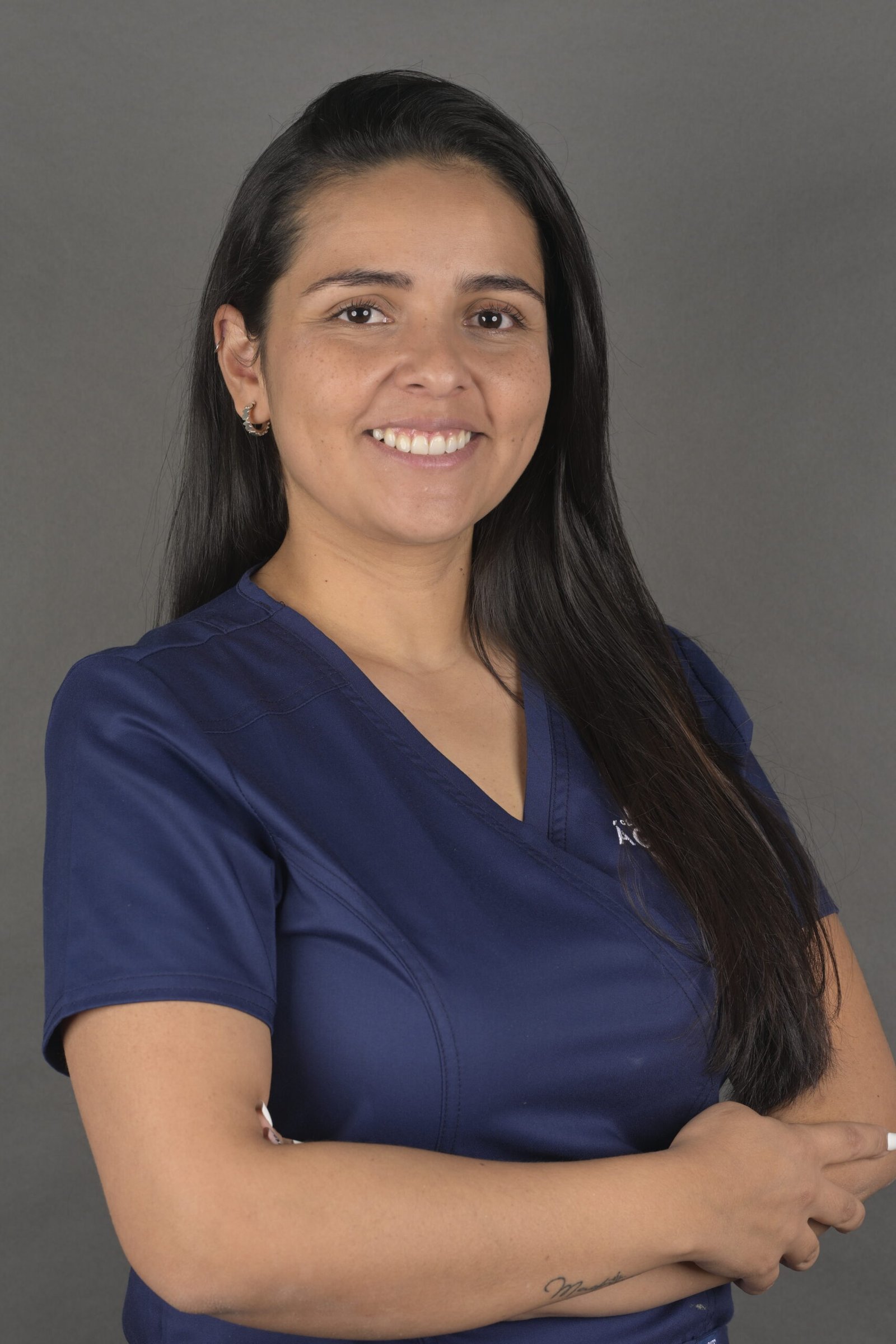 Retrato profesional de Érika Montoya Cardona, higienista dental en Clínica Dental Ágora, con uniforme clínico y los brazos cruzados frente a un fondo gris